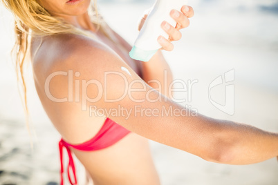 Mid-section of woman applying sunscreen lotion on the beach