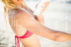 Mid-section of woman applying sunscreen lotion on the beach