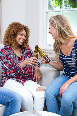 Female friends toasting beer while sitting on sofa