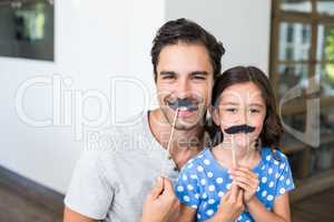 Smiling father and daughter with artificial mustache