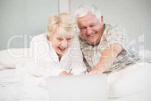 Couple laughing while using laptop in bed