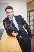 Businessman using cellphone while leaning on counter at office