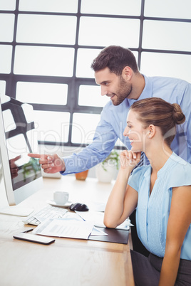 Businessman pointing at computer while explaining female colleag