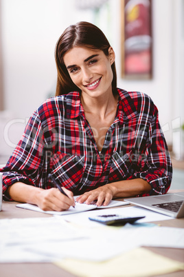 Portrait of smiling woman writing in notepad with laptop Portrait of smiling woman writing in notepad with laptop