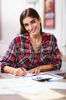 Portrait of smiling woman writing in notepad with laptop