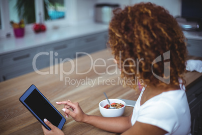 Woman using digital tablet while sitting in kitchen