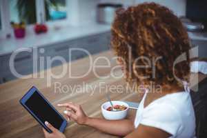 Woman using digital tablet while sitting in kitchen