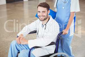 Portrait of smiling doctor sitting on wheelchair with colleague