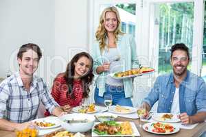 Portrait of smiling woman serving food to friends