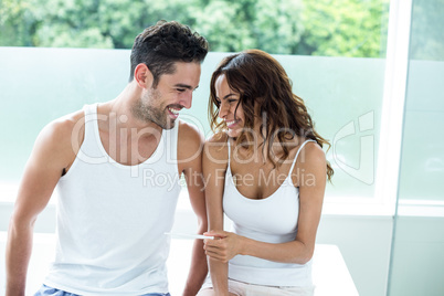 Woman holding pregnancy kit while sitting beside husband