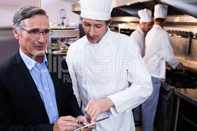 Male restaurant manager writing on clipboard while interacting t