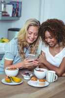 Female friends using cellphone during breakfast
