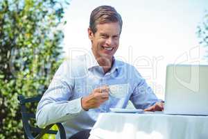 Casual businessman having coffee and using laptop