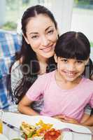 Smiling mother and daughter sitting at dining table