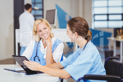 Female doctor sitting on wheelchair while using digital tablet w