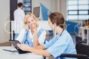 Female doctor sitting on wheelchair while using digital tablet w