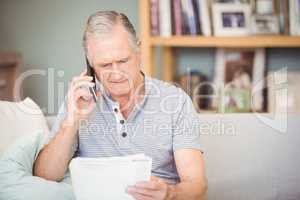 Senior man using mobile phone while looking documents