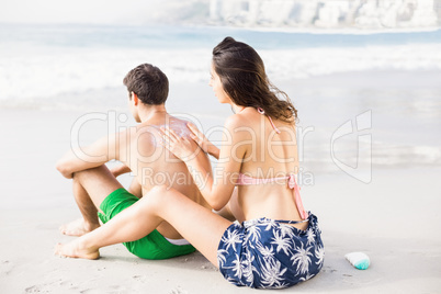 Woman applying sunscreen lotion on mans back