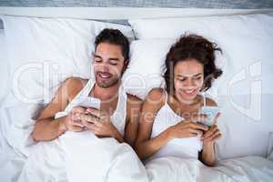 High angle view of couple using smartphone on bed