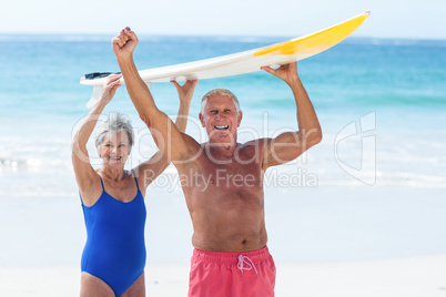 Cute mature couple holding a surfboard over their heads