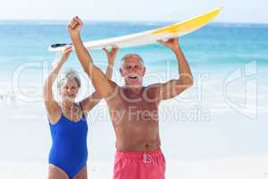 Cute mature couple holding a surfboard over their heads