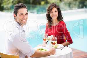 Portrait of smiling couple sitting by swimming pool