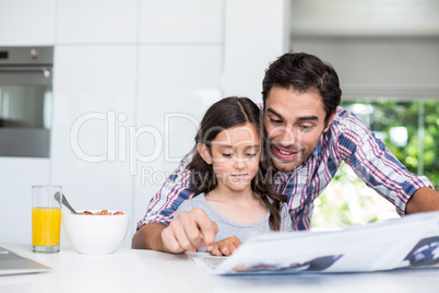 Father and daughter reading newspaper at home