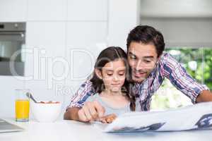 Father and daughter reading newspaper at home