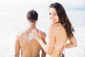 Woman applying sunscreen lotion on mans back