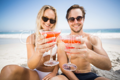 Young couple in sunglasses showing cocktail glass on the beach