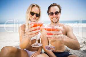 Young couple in sunglasses showing cocktail glass on the beach