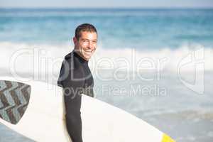 Portrait of happy man holding a surfboard on the beach