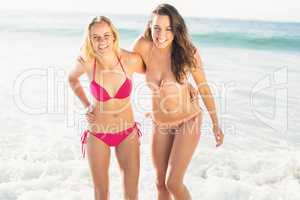 Portrait of two happy women in bikini standing on the beach