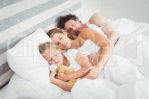 High angle view of parents sleeping with daughter on bed