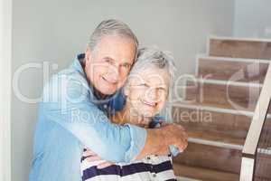 Portrait of cheerful senior couple embracing on staircase