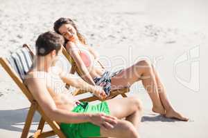 Young couple sitting on armchair and relaxing on the beach