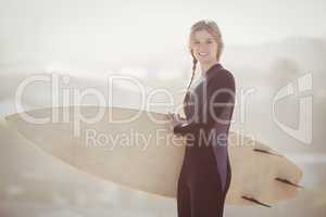 Happy woman in wetsuit holding a surfboard on the beach