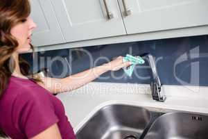 Woman wiping faucet at kitchen sink