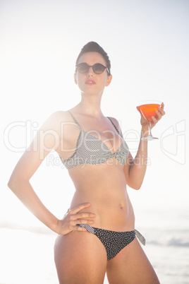 Glamorous woman with a cocktail drink standing on the beach
