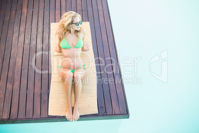 Beautiful woman in green bikini relaxing by poolside