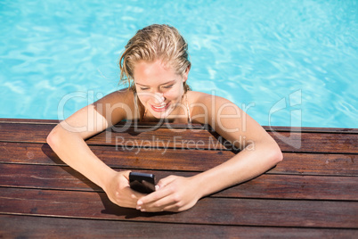 Beautiful woman leaning on poolside and typing a text message