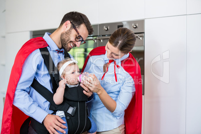 Couple in superhero costume feeding milk to daughter