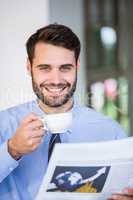 Confident businessman holding coffee cup and newspaper