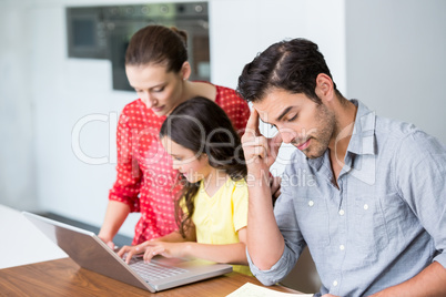 Daughter and mother working on laptop with tensed father sitting