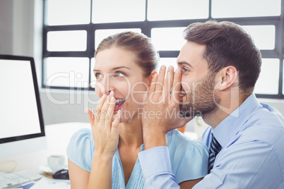 Happy businessman whispering to female colleague