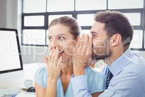 Happy businessman whispering to female colleague