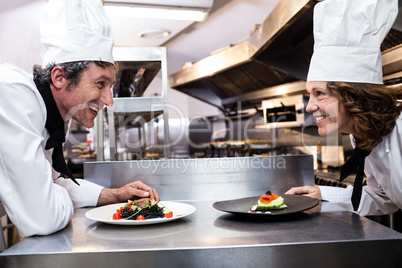 Two smiling chefs leaning on counter with meal plates