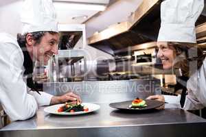 Two smiling chefs leaning on counter with meal plates