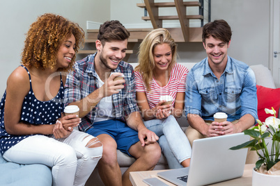 Friends with drinks looking in laptop while sitting on sofa