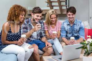 Friends with drinks looking in laptop while sitting on sofa